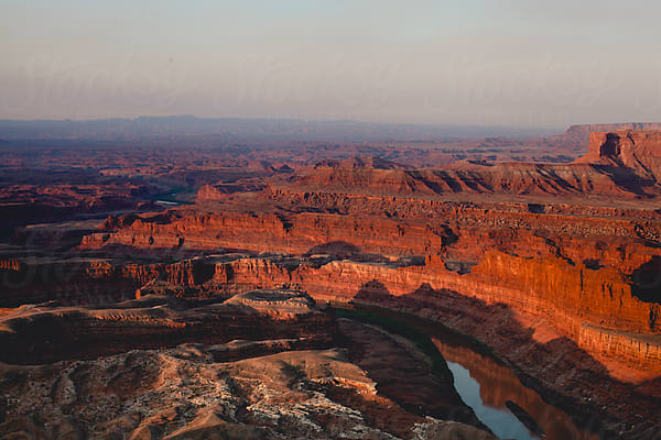 Deep canyon at first light, geological strata illuminated in red and amber, river bend visible at the canyon floor.